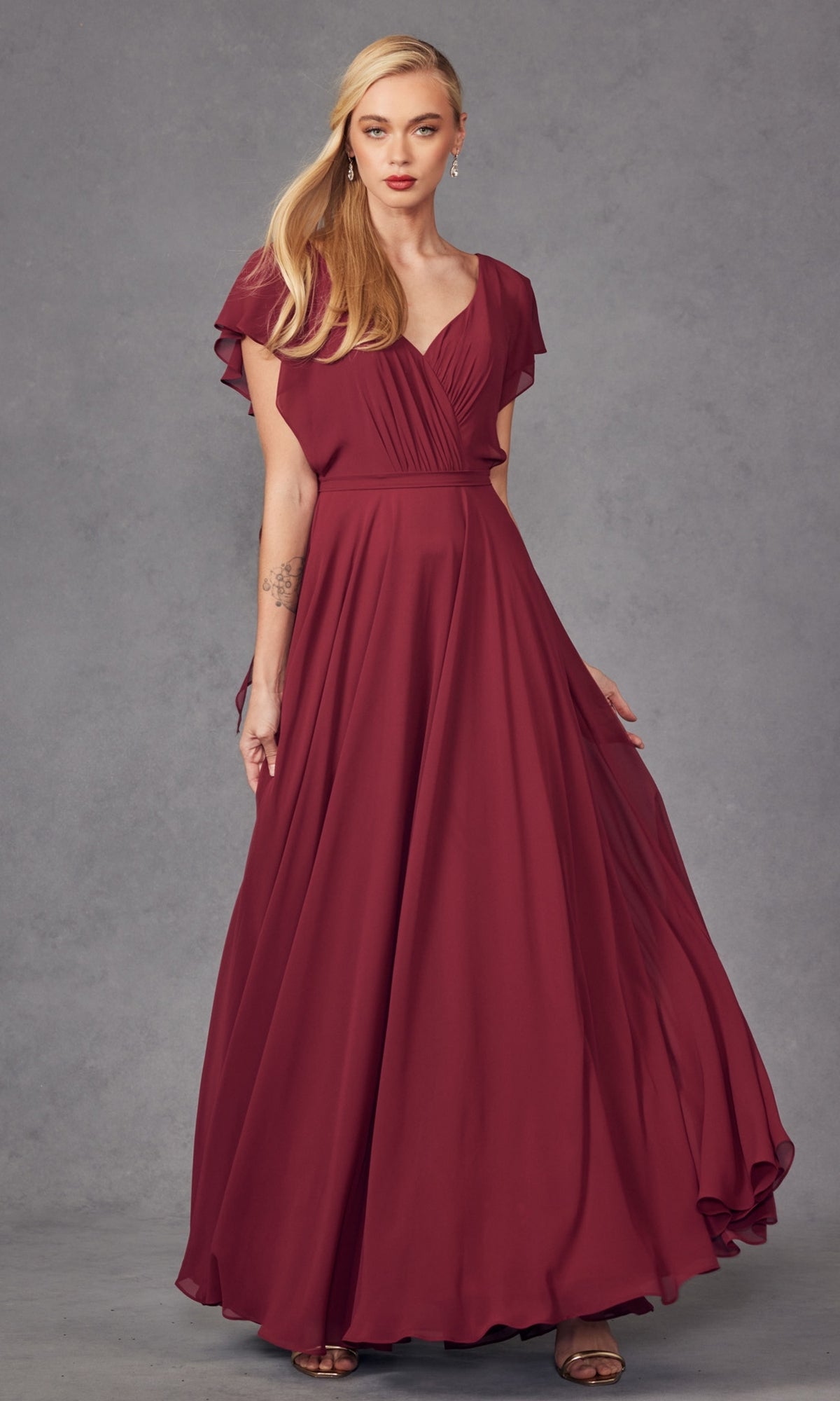 A woman stands against a plain gray background wearing the Flutter-Sleeve Long Formal Evening Gown 261, a floor-length, deep red A-line dress featuring flutter sleeves and a v-neckline.